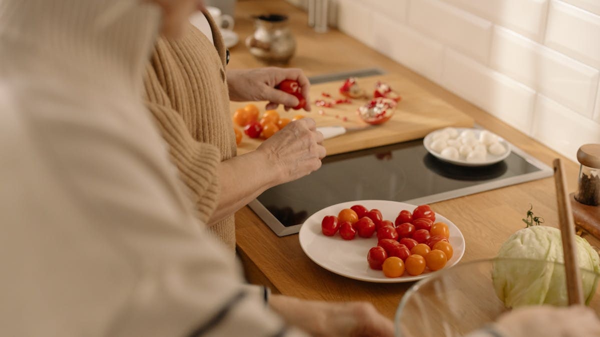 Two adults prepare a fresh salad with cherry tomatoes and cabbage in a warm, inviting kitchen.